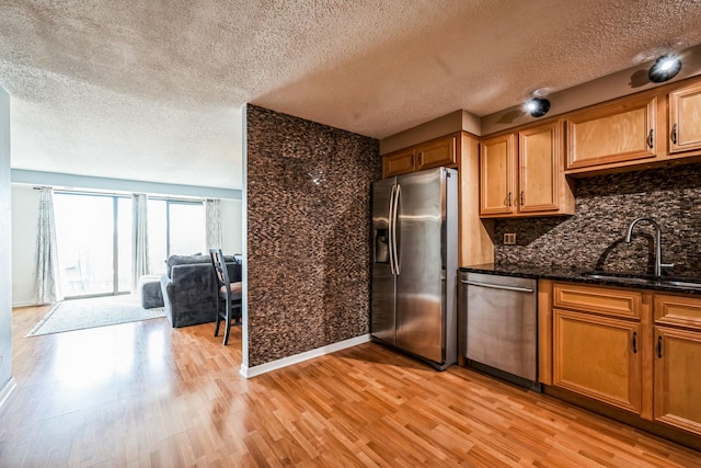 kitchen featuring sink, tasteful backsplash, dark stone countertops, stainless steel appliances, and light hardwood / wood-style floors