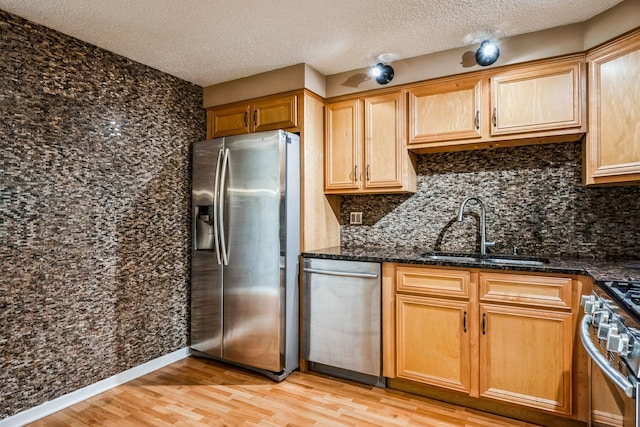 kitchen featuring sink, dark stone countertops, light hardwood / wood-style floors, stainless steel appliances, and a textured ceiling