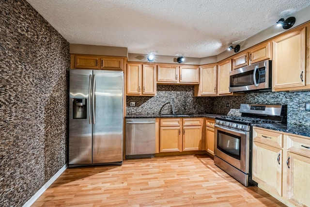 kitchen featuring sink, stainless steel appliances, light hardwood / wood-style floors, a textured ceiling, and dark stone counters