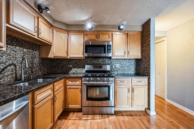 kitchen with sink, appliances with stainless steel finishes, a textured ceiling, dark stone counters, and light wood-type flooring