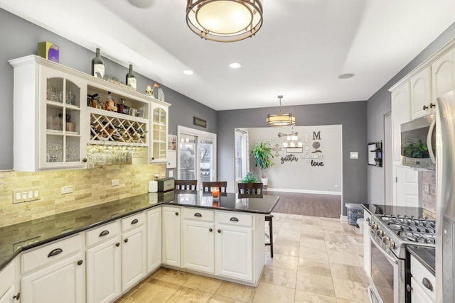 kitchen with hanging light fixtures, white cabinets, decorative backsplash, stainless steel range with gas cooktop, and kitchen peninsula