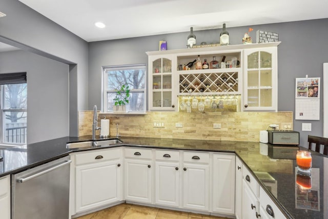 kitchen featuring sink, white cabinetry, dark stone countertops, tasteful backsplash, and stainless steel dishwasher