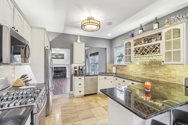 kitchen with sink, white cabinetry, stainless steel appliances, kitchen peninsula, and dark stone counters