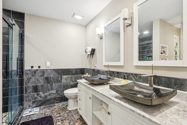 bathroom with vanity, toilet, a shower with shower door, and tile walls