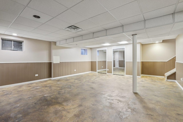 basement with a paneled ceiling and wood walls