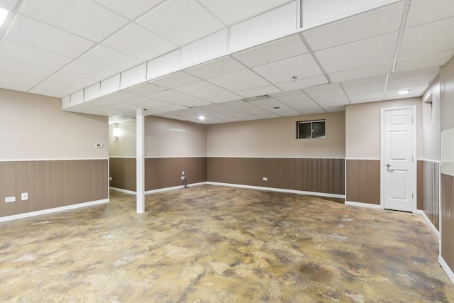 basement featuring a drop ceiling and wooden walls