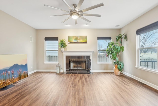 unfurnished living room featuring hardwood / wood-style floors, a tile fireplace, a healthy amount of sunlight, and ceiling fan