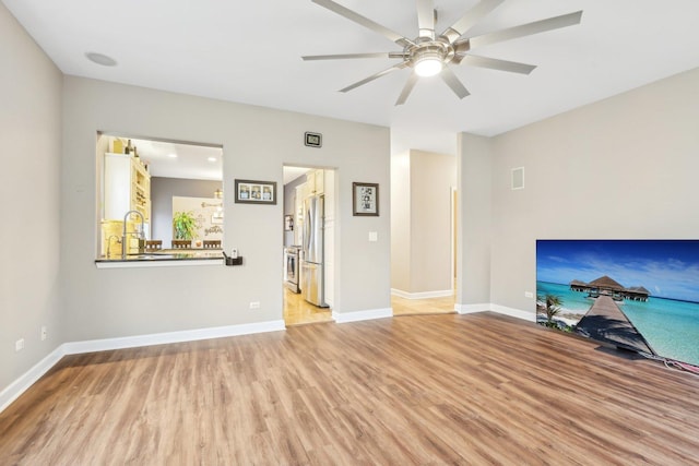 unfurnished living room featuring ceiling fan, sink, and light wood-type flooring