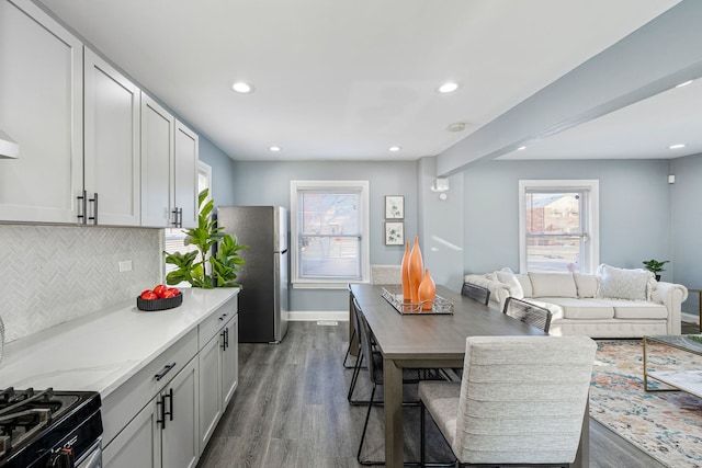 kitchen with white cabinets, stainless steel fridge, dark hardwood / wood-style flooring, light stone counters, and a healthy amount of sunlight