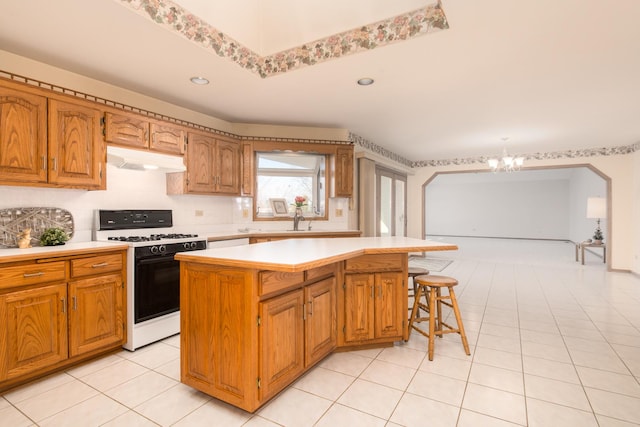 kitchen featuring light tile patterned flooring, tasteful backsplash, a kitchen island, a notable chandelier, and gas range oven