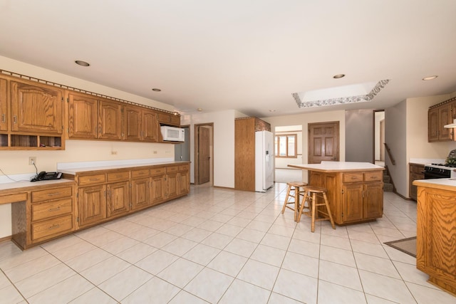 kitchen featuring a kitchen island, built in desk, a breakfast bar area, light tile patterned floors, and white appliances