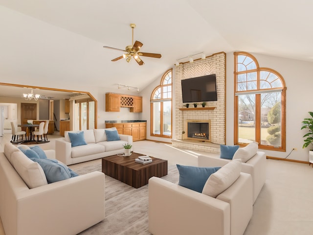 carpeted living room with a brick fireplace, ceiling fan with notable chandelier, high vaulted ceiling, and rail lighting