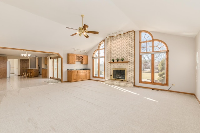 unfurnished living room with ceiling fan with notable chandelier, light carpet, high vaulted ceiling, and a brick fireplace