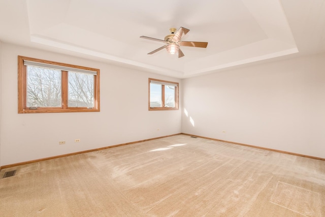 empty room featuring light colored carpet, ceiling fan, and a tray ceiling