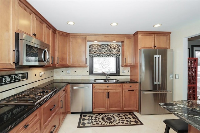 kitchen with sink, backsplash, dark stone counters, light tile patterned floors, and stainless steel appliances