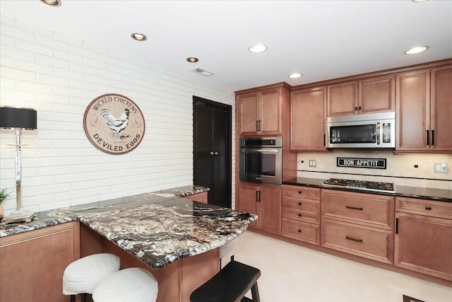 kitchen with dark stone countertops, decorative backsplash, a kitchen breakfast bar, and appliances with stainless steel finishes