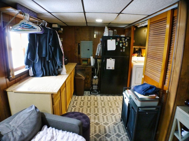 kitchen with a paneled ceiling, wooden walls, electric panel, black fridge, and washer / dryer