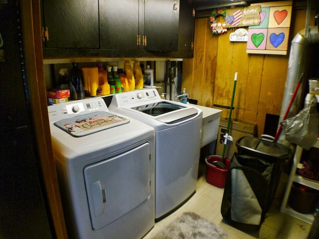 clothes washing area featuring cabinets, sink, wood walls, and washing machine and clothes dryer