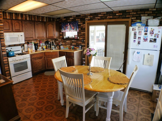 kitchen with brick wall, sink, a drop ceiling, and white appliances