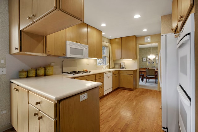 kitchen featuring light brown cabinetry, a notable chandelier, kitchen peninsula, white appliances, and light hardwood / wood-style flooring