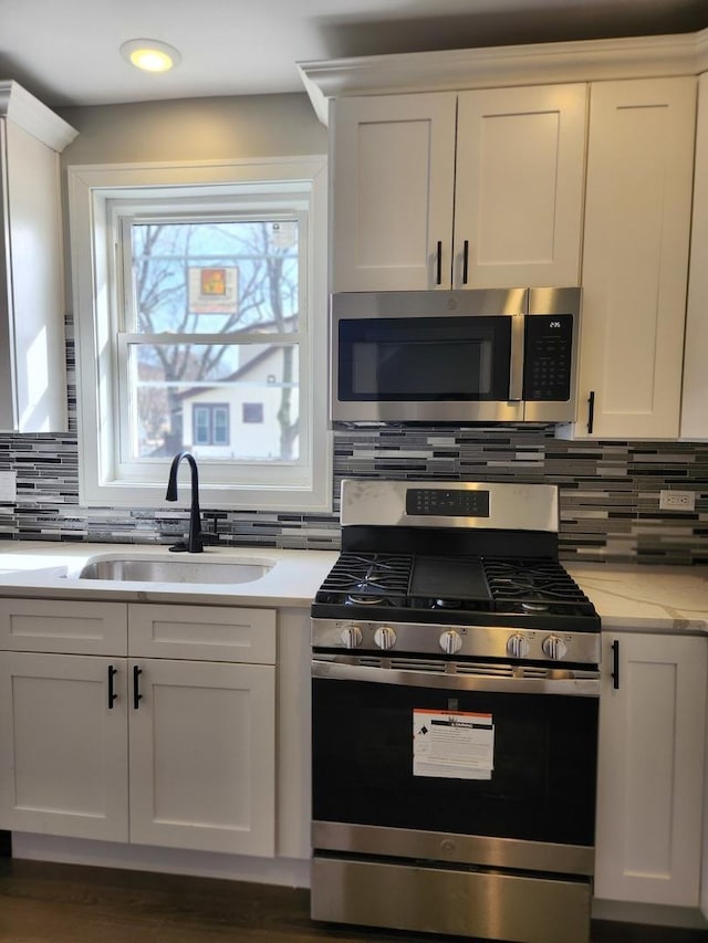 kitchen with sink, light stone counters, stainless steel appliances, decorative backsplash, and white cabinets