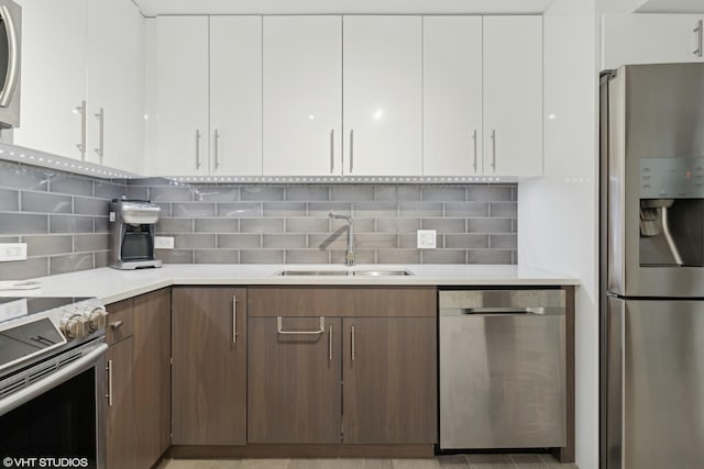 kitchen with stainless steel appliances, white cabinetry, sink, and backsplash