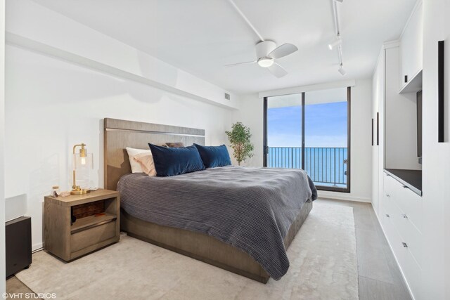 bedroom with a wall of windows, rail lighting, ceiling fan, wood-type flooring, and access to outside