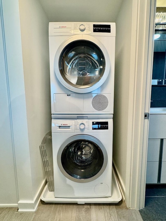 laundry area with stacked washer and dryer and light wood-type flooring