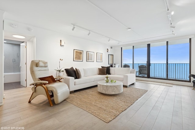 living room with a water view, track lighting, floor to ceiling windows, and light wood-type flooring