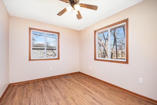 spare room with a ceiling fan, light wood-type flooring, visible vents, and baseboards