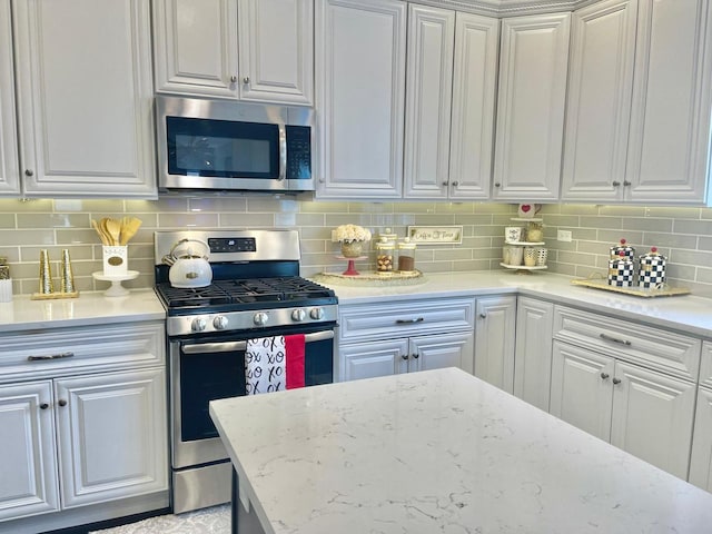 kitchen with white cabinetry, appliances with stainless steel finishes, light stone countertops, and decorative backsplash