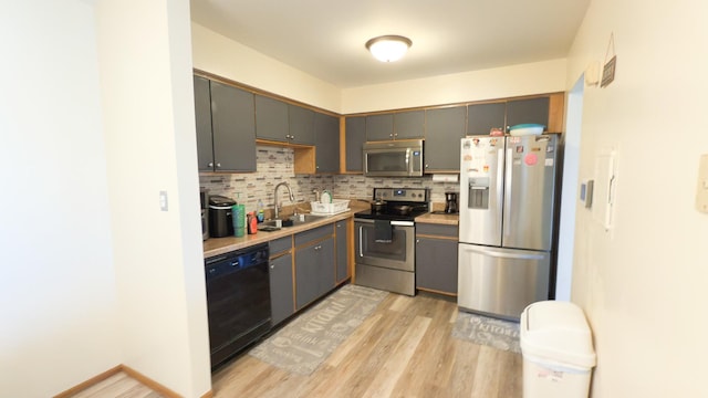 kitchen featuring tasteful backsplash, sink, gray cabinetry, stainless steel appliances, and light hardwood / wood-style flooring