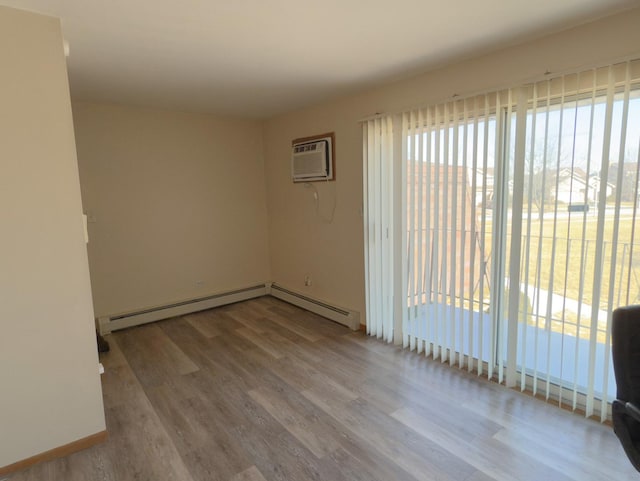 spare room featuring an AC wall unit, baseboard heating, and wood finished floors