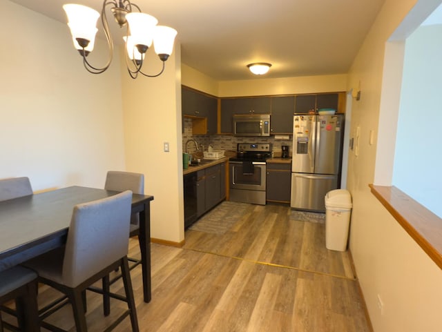 kitchen featuring appliances with stainless steel finishes, a sink, an inviting chandelier, light wood-style floors, and backsplash