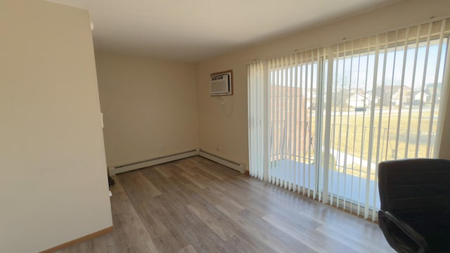 empty room with baseboard heating, a wall mounted AC, and light hardwood / wood-style flooring