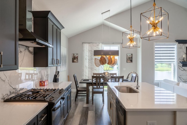 kitchen featuring wall chimney exhaust hood, gas range, hanging light fixtures, a center island with sink, and plenty of natural light