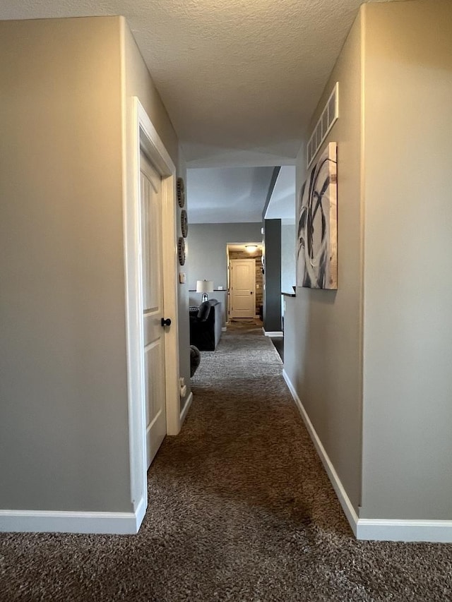 corridor with a textured ceiling and dark colored carpet