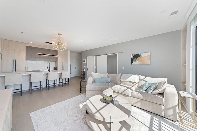 living room featuring a notable chandelier, light wood-style floors, and visible vents