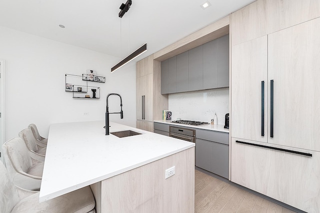 kitchen featuring gray cabinetry, a sink, light countertops, stainless steel gas stovetop, and light wood-style floors
