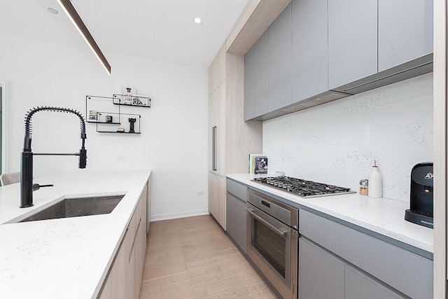kitchen with appliances with stainless steel finishes, light wood-style floors, gray cabinetry, and a sink
