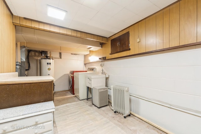 laundry room with independent washer and dryer, radiator heating unit, water heater, and wood walls