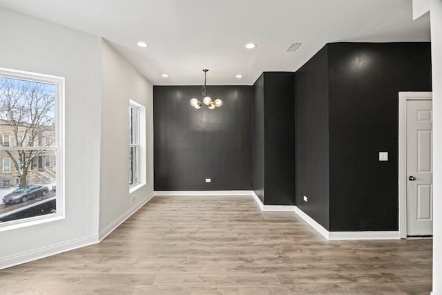 unfurnished room featuring light wood-type flooring, a wealth of natural light, and a chandelier