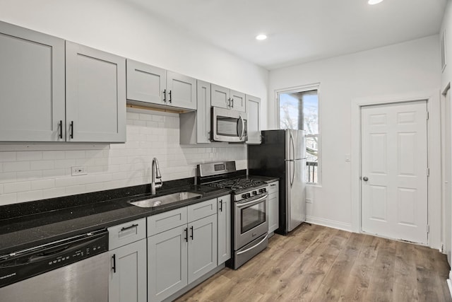 kitchen with sink, dark stone countertops, gray cabinets, stainless steel appliances, and light hardwood / wood-style floors