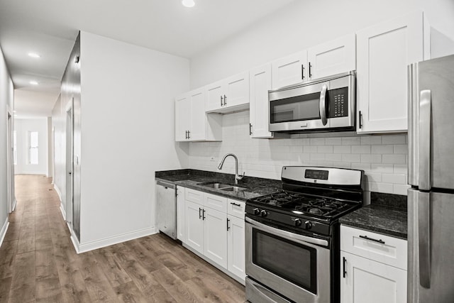 kitchen with sink, light hardwood / wood-style flooring, appliances with stainless steel finishes, white cabinets, and dark stone counters