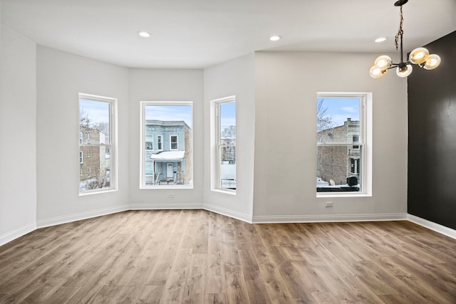 spare room with a notable chandelier, hardwood / wood-style flooring, and a healthy amount of sunlight