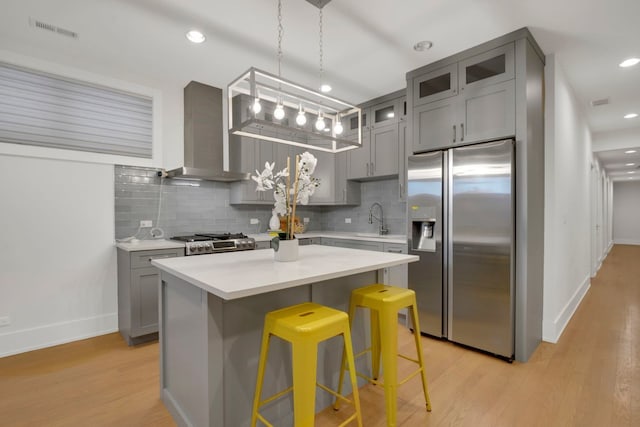 kitchen featuring decorative backsplash, a center island, light hardwood / wood-style floors, stainless steel appliances, and wall chimney range hood