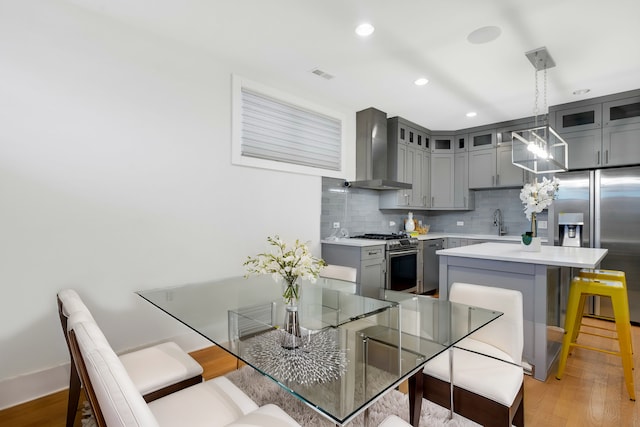 kitchen featuring sink, appliances with stainless steel finishes, hanging light fixtures, tasteful backsplash, and wall chimney exhaust hood