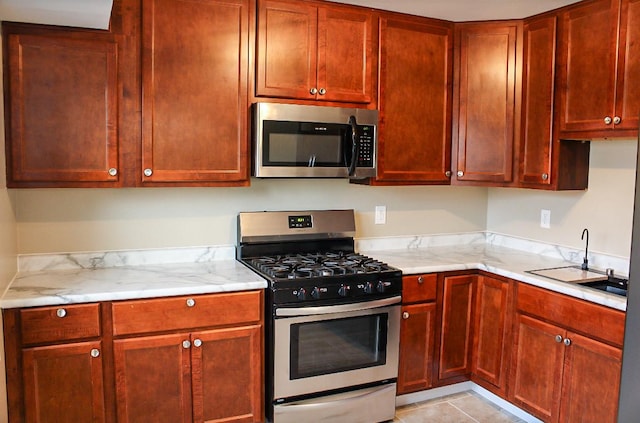 kitchen with appliances with stainless steel finishes, sink, light tile patterned floors, and light stone counters