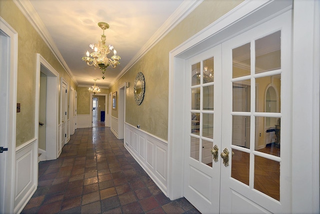 hallway with ornamental molding, a decorative wall, a wainscoted wall, french doors, and a notable chandelier