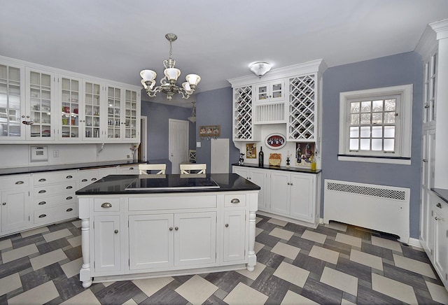 kitchen featuring dark countertops, black electric stovetop, a chandelier, radiator, and white cabinetry
